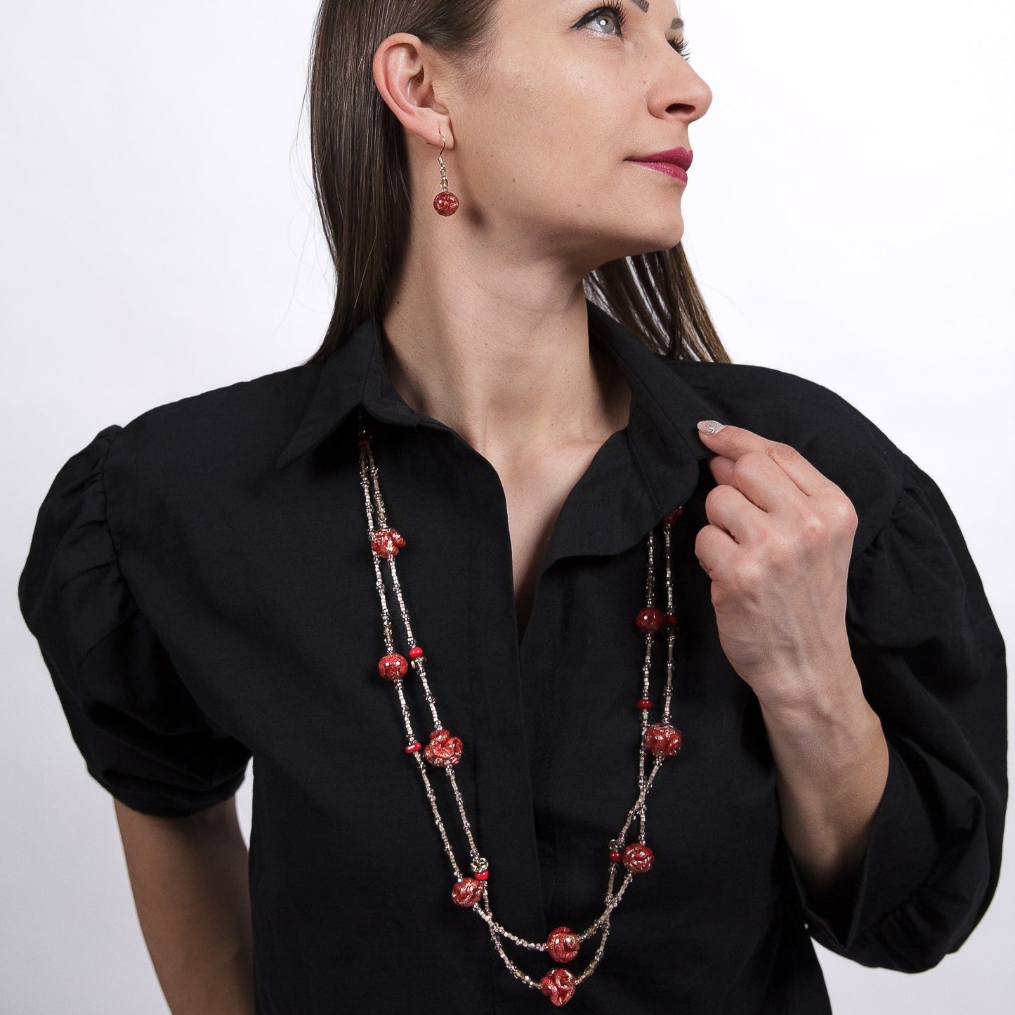 Woman wearing a black blouse with a long red beaded necklace against a white background