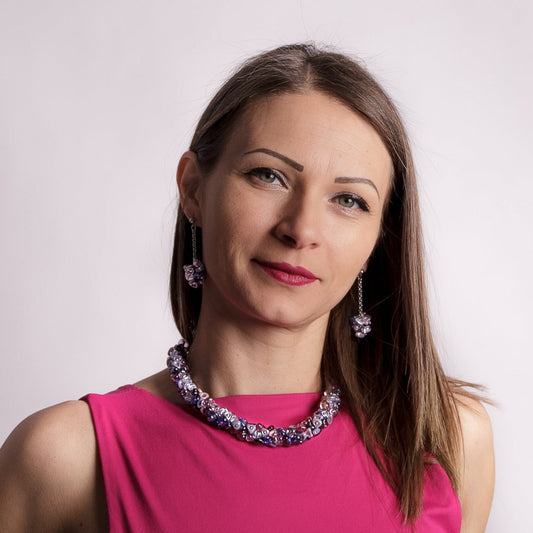 Woman wearing a pink dress with a floral necklace and earrings against a light background
